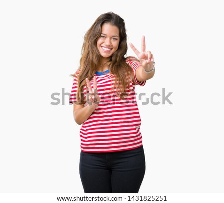 Young beautiful brunette woman wearing stripes t-shirt over isolated background smiling looking to the camera showing fingers doing victory sign. Number two.