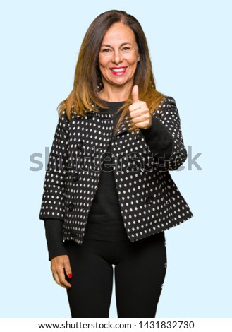Beautiful middle age woman wearing fashion jacket doing happy thumbs up gesture with hand. Approving expression looking at the camera showing success.