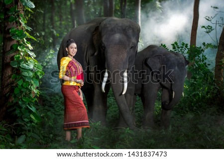 Young women in Thai folk costumes stand together with elephants.