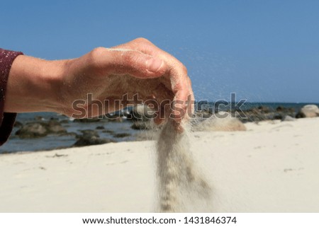 a handful of fine sand, the sand trickles away between the fingers, the sand trickles toward the beach