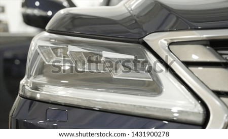Close up for the headlights of the black new, polished car, luxury concept. Action. Modern car headlights parked in a dealer showroom.