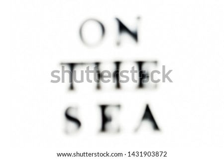 The inscription ON THE SEA. ON THE SEA in black blurred letters on a white background. Photo of the lettering, close-up