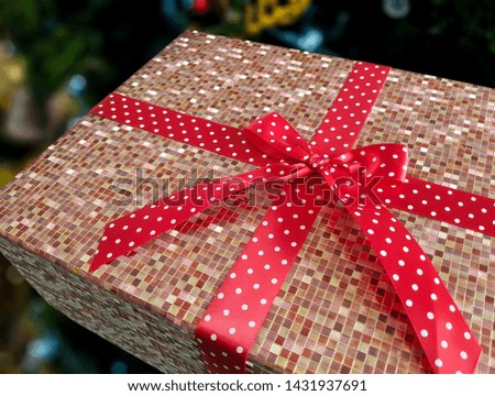 Gift box in the celebration wrapped in brown square pattern, Tied with a red ribbon with white dots.
