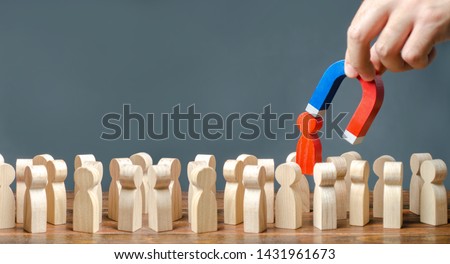 A hand with a magnet pulls a red human figure out of the crowd. Identify disloyal, repression, dissent. toxic, non-competent worker. leader manages the business. Search for enemies and spies. Royalty-Free Stock Photo #1431961673