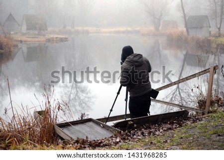 Photographer on assignment, holding a camera, taking photos of the beautiful lake in the morning.