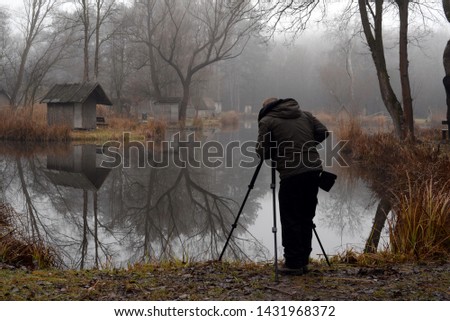 Photographer on assignment, holding a camera, taking photos of the beautiful lake in the morning.