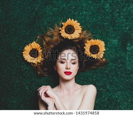Portrait of beautiful red-haired girl with sunflowers on green grass. Above view