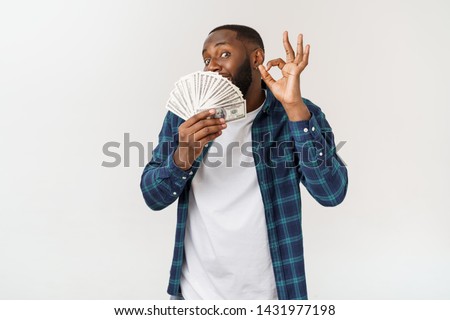 Portrait of young smiling dark skin african american man in white t shirt holding money and showing okay sign isolated on gray background