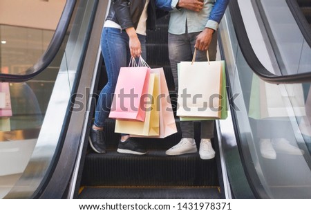 Unrecognizable african couple with shopping bags rising on escalator in mall center, panorama