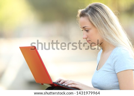 Side view portrait of a serious teenage girl using a red laptop sitting in a park