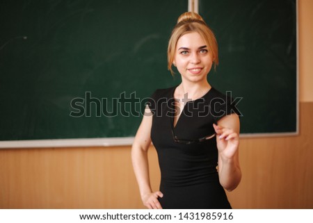 Young female teacher in glasses stand in front of blackboard