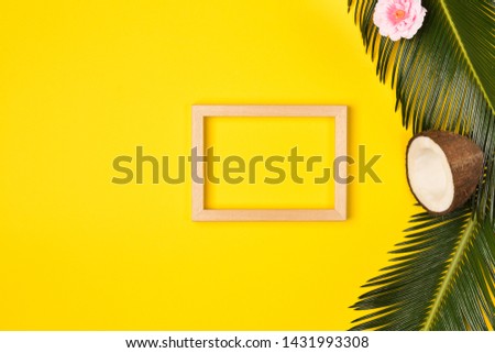 Stylish summer composition with photo frame, green leaves, flower and coconut on a yellow background. Artwork mockup with copy space