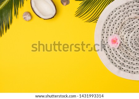 Stylish summer composition coconut, green leaves, hat and seashells on yellow background. Artwork mockup with copy space