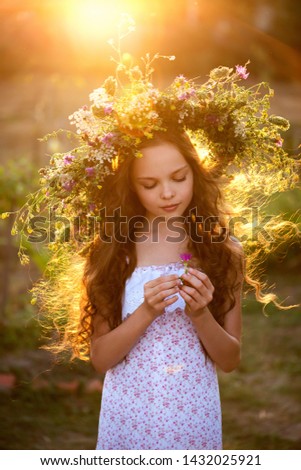 Cute smiling little girl with flower wreath on the meadow at the farm. Portrait of adorable small kid outdoors. Midsummer.