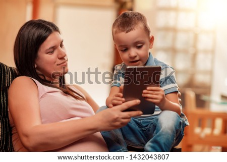 Pregnant woman and her son watching cartoons on tablet.