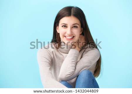studio portrait of a beautful caucasian woman, sitting on floor, looking at camera smiling, isolated on blue background