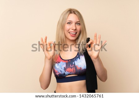 Young blonde sport woman over isolated wall showing an ok sign with fingers