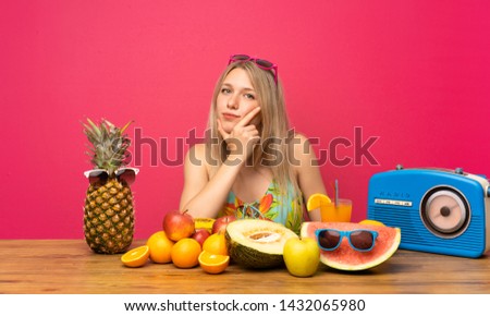 Young blonde woman with lots of fruits thinking an idea