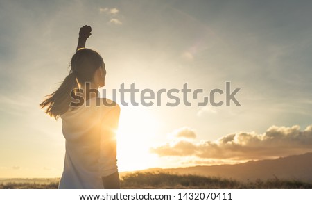 Strong, determined, confident woman with her fist up in the air facing sunset. Royalty-Free Stock Photo #1432070411