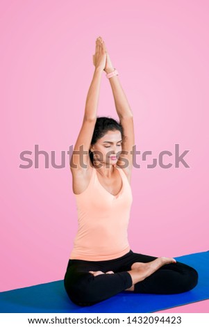 Picture of curly hair woman lifting hands while doing yoga exercise in the studio