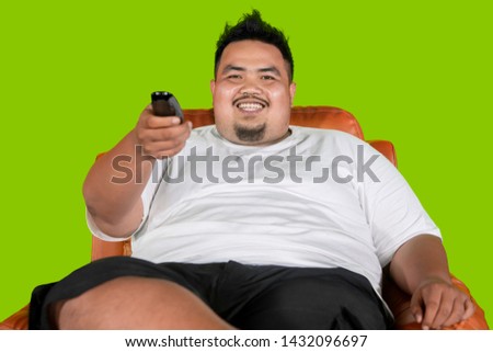 Picture of a happy fat man watching television while sitting in the armchair with green screen