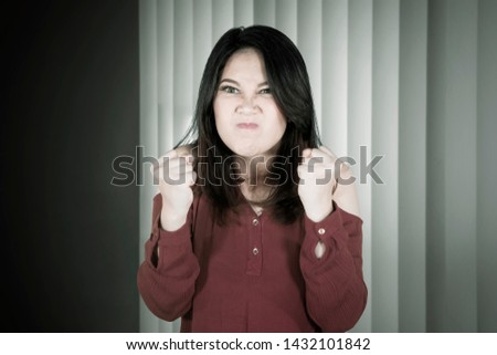 Picture of young Asian woman looks angry while clenching her fists near the window