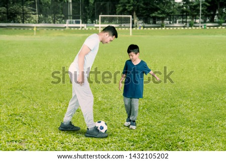 Picture of young father playing football with his son in the soccer field 