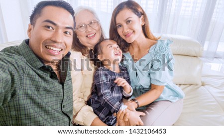 Cheerful three generation family sitting on the sofa while taking a group selfie picture at home