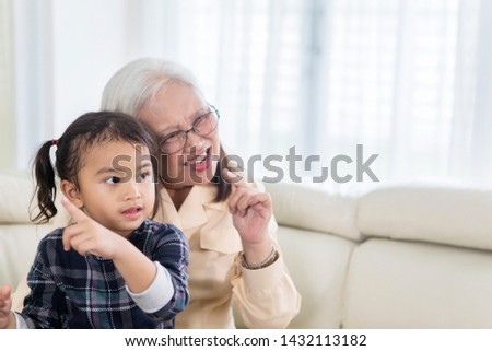 Picture of cheerful old woman watching TV with her grandchild at home