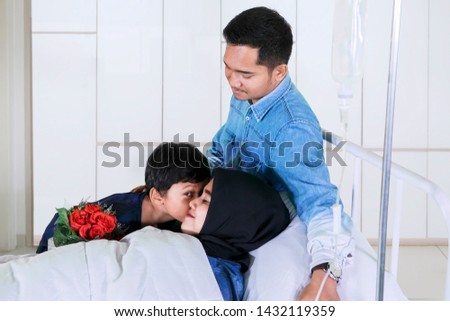 Picture of sick young mother kissed by her son while lying on the bed. Shot in the hospital