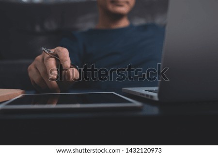 Casual business man with pen in hand sitting at wooden desk, looking on laptop computer screen with digital tablet on wooden desk. Freelancer working from home, close up. Business ,technology concept