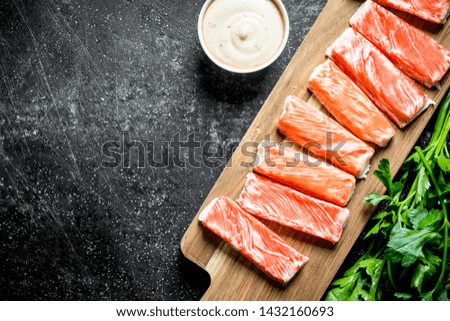 Crab sticks on a cutting Board with sauce and parsley. On dark rustic background