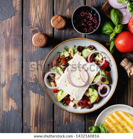 Feta cheese salad in ceramic bowl served with olives, tomatoes, onions, coriander, olive oil, halloumi cheese and basil over dark wooden background. Top view, flat lay. Square image