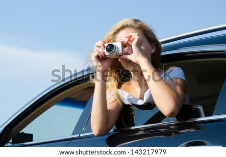Woman photographer leaning out of car window taking a photo with a compact digital camera