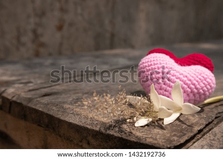 Red and pink knitting hearts with Millingonia on the wooden rough table. Background of the rock wall. Sun light shines on the frame. Copy space for editing and text.