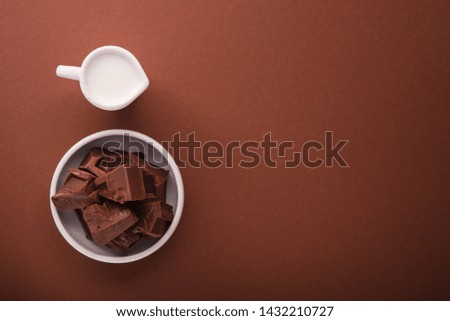 Pieces of chocolate and a carafe of milk on a brown color background. Top view. place for text