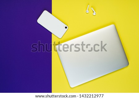 Closed Laptop Phone Earphone Freelance Workplace Top View Copy Space. White Smartphone and Airpod on Minimal Clear Business Yellow Purple Background. Programmer Work Instrument Equipment Concept Royalty-Free Stock Photo #1432212977