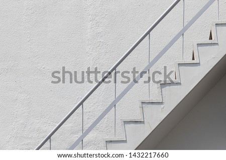 side view of old white outside fire escape emergency staircase with metal handrail railing and concrete wall. Royalty-Free Stock Photo #1432217660