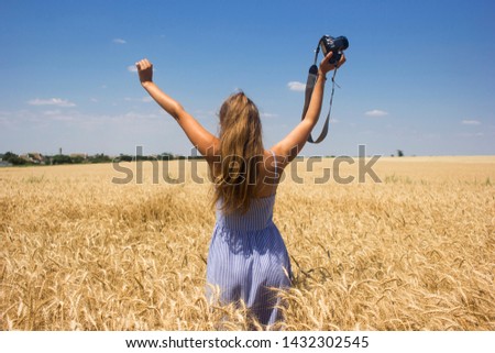Woman in a blue dress with a camera on a wheat field. Standing with his hands up. The concept of freedom of thinking and creativity, lifestyle

