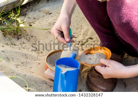 Girl in maroon tights plays with toys in a sandbox.