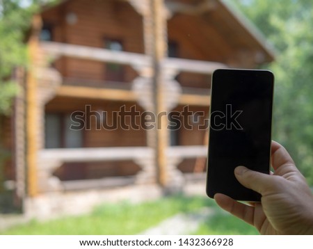 Hand with a phone in the background of a country house