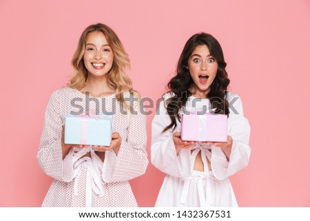 Image of excited happy young two pretty women girls friends sisters posing isolated over pink wall background holding present boxes.