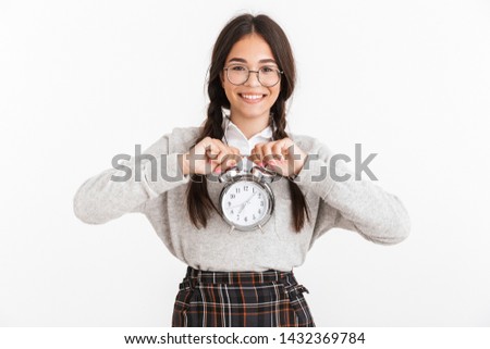 Photo closeup of pretty teenage girl wearing eyeglasses smiling while holding alarm clock in hands isolated over white background