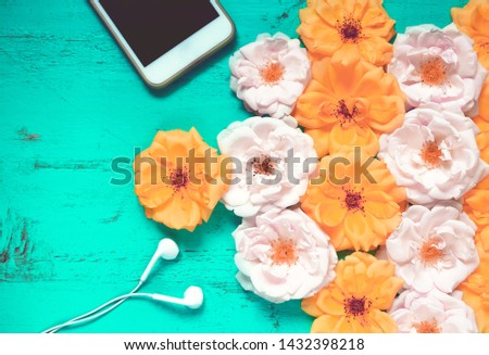Beautiful summer background with fresh roses, smartphone and white earphones on an old painted wooden table for blogs, web design, posters, seasonal cards and business concepts
