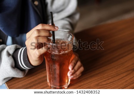Women hand with ice tea in a glass at the cafe. Ice tea drink using plastic straw. Royalty-Free Stock Photo #1432408352