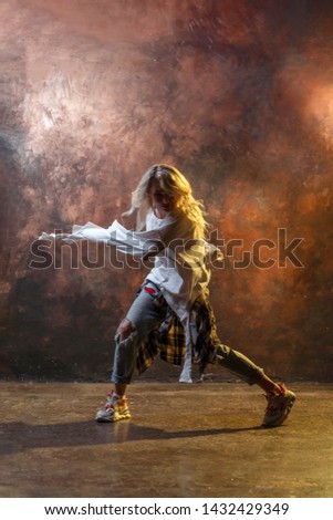 Image of dancing long-haired blonde girl in torn blue jeans on brown background
