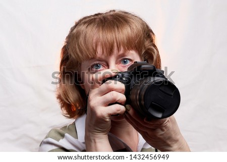 Blonde-haired female photographer with photo camera in her hands on a white background. Woman taking a photo