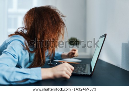 A woman with disheveled hair sits in front of an open laptop indoors working at home Royalty-Free Stock Photo #1432469573