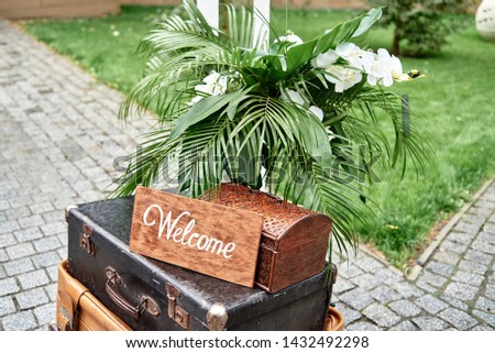 Wedding decorations with welcome sign board, flowers, pulm leaves and vintage suitcases in garden, copy space