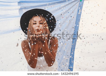 pretty woman with colorful straw hat blowing confetti in the middle of clothes hanging out to dry on a terrace in the city
